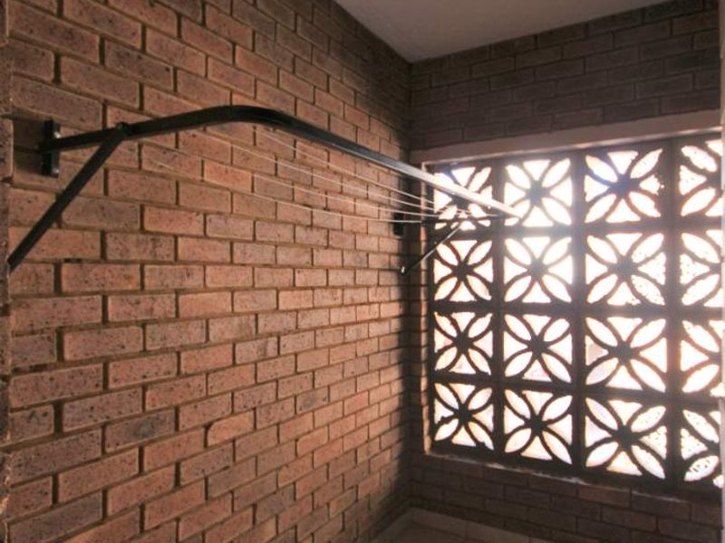 A functional laundry area featuring exposed brick walls, tiled flooring, and a decorative breeze block screen for ventilation.