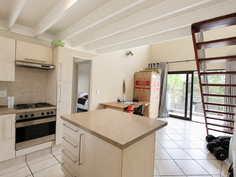 Open-plan kitchen and living area featuring light wood cabinetry, stone-look countertops, tiled floors, exposed beam ceilings, and direct access to a balcony via sliding doors.