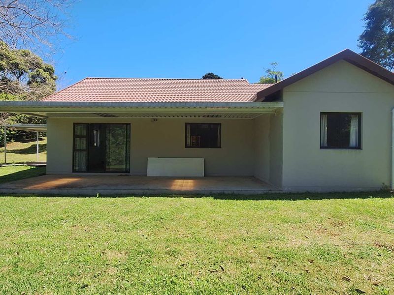 Rear view of the house featuring a covered patio, tiled roof, and a spacious garden area with established trees.