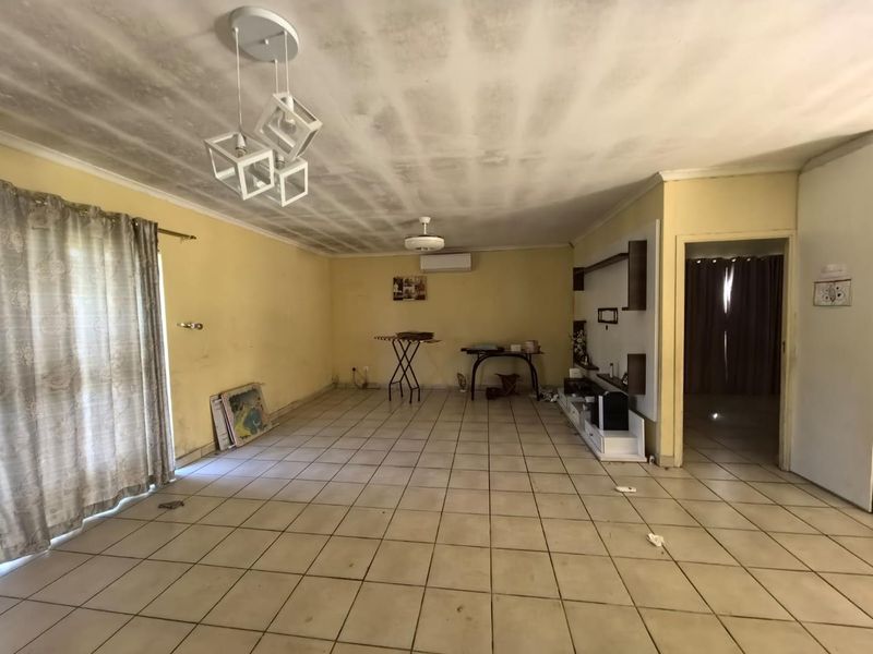Spacious living area featuring ceramic floor tiles, a built-in shelving unit, and a split-system air conditioner, requiring cosmetic updates to the ceiling and walls.