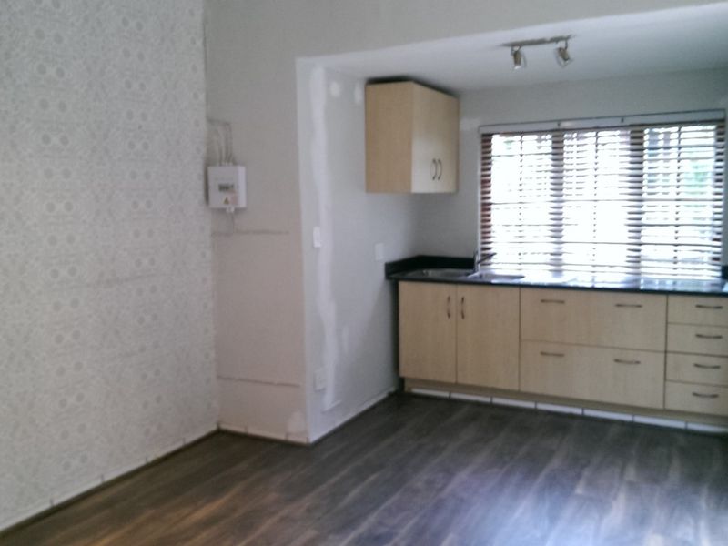 Open plan office space featuring laminate flooring, built-in cabinetry, and venetian blinds, currently requiring minor wall finishing and cosmetic updates.