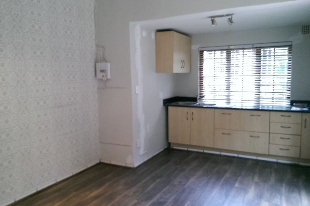 Open plan office space featuring laminate flooring, built-in cabinetry, and venetian blinds, currently requiring minor wall finishing and cosmetic updates.
