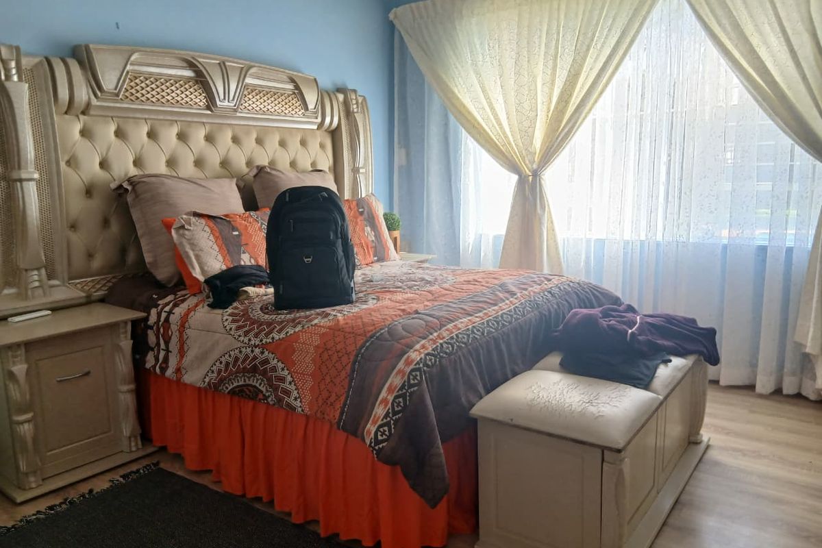 A bedroom featuring light-toned wood-look flooring, a large window with sheer curtains, and a neutral wall color.