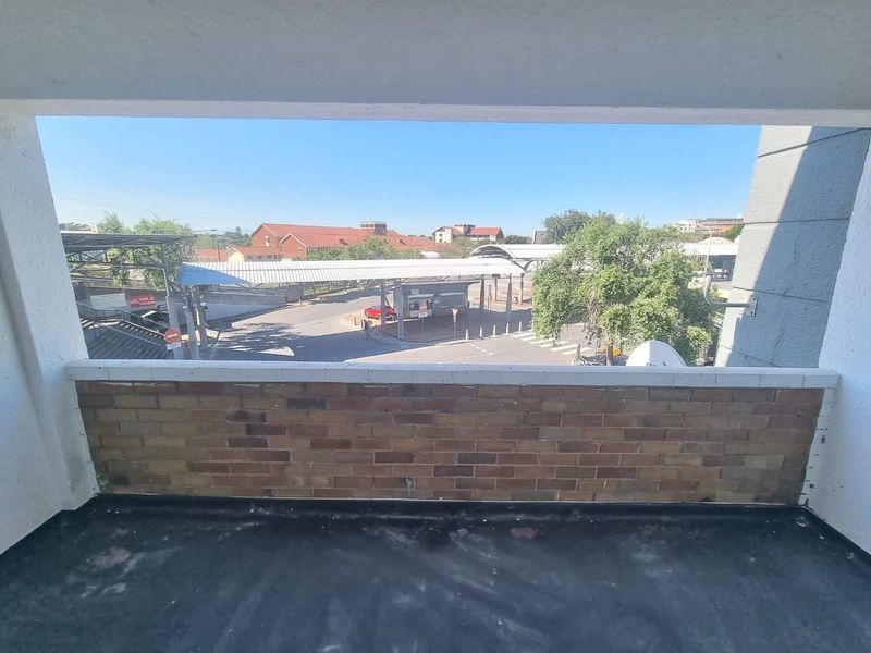 An open-air balcony featuring a brick balustrade and concrete flooring, offering an elevated view of the surrounding street and neighborhood infrastructure.