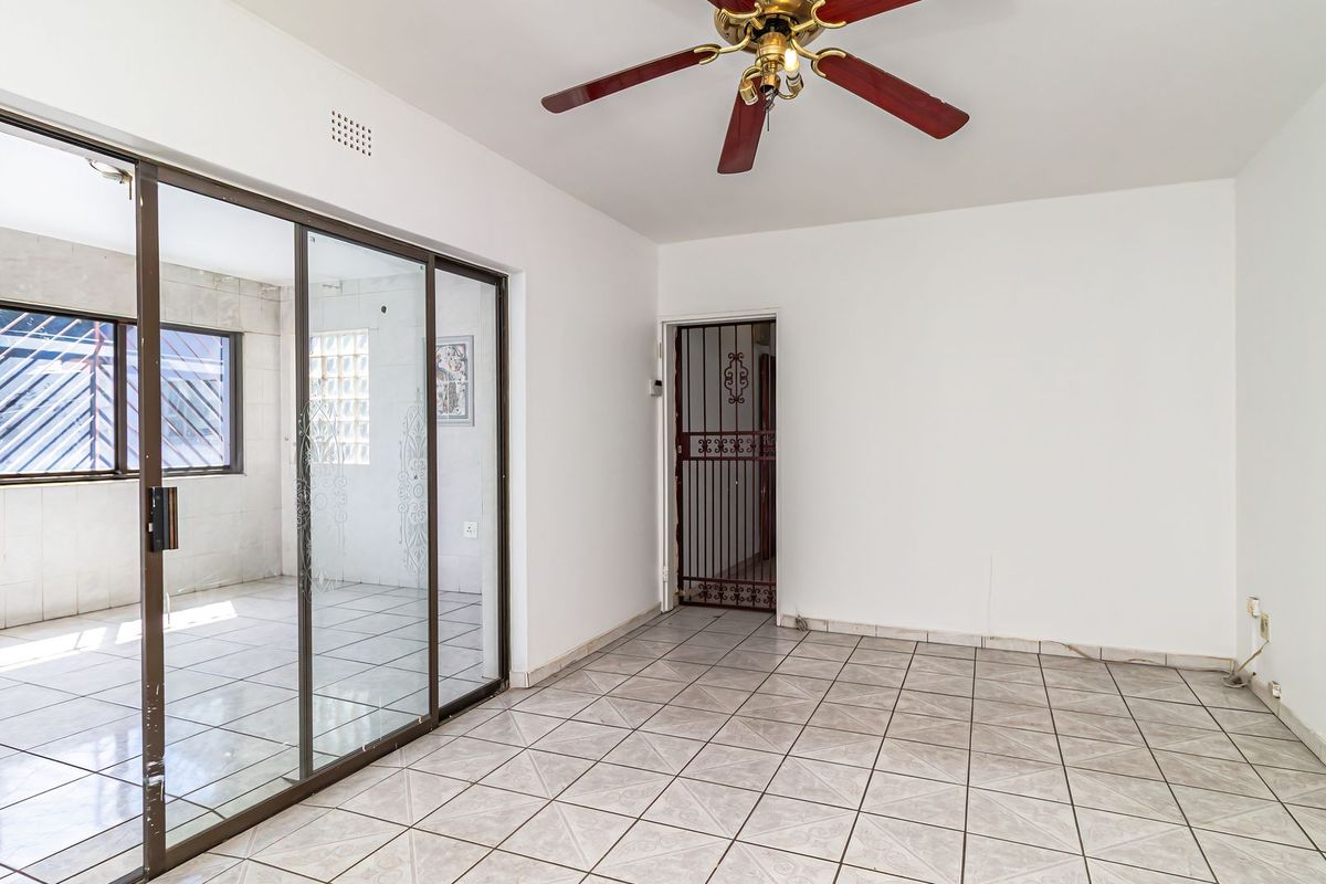 An empty living area featuring tiled flooring, a ceiling fan, and a large sliding glass door leading to an adjacent tiled sunroom or patio space.