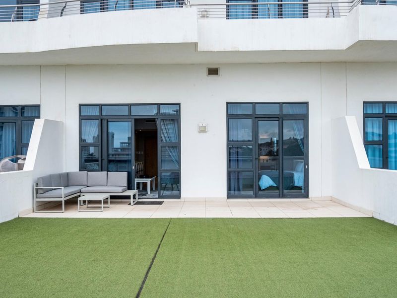 A spacious ground-floor patio featuring tiled flooring, artificial grass, and multiple aluminium-framed glass sliding doors providing access to the interior.
