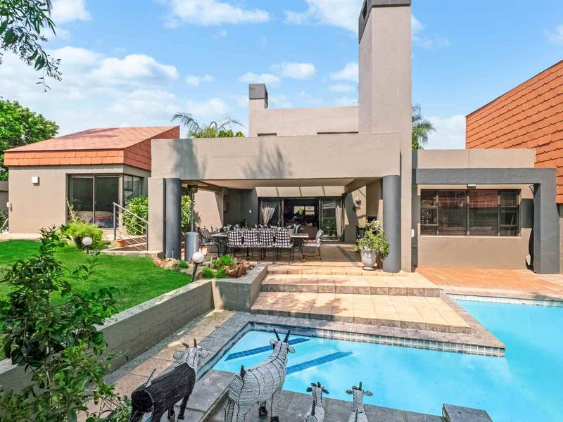 Rear view of the property featuring a covered patio, tiled terrace, and a swimming pool set within a landscaped garden.