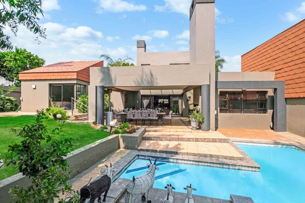 Rear view of the property featuring a covered patio, tiled terrace, and a swimming pool set within a landscaped garden.