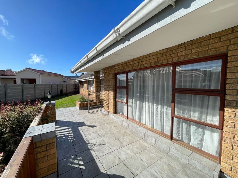 A spacious covered patio featuring tiled flooring, brick accents, and direct access to the rear garden area.