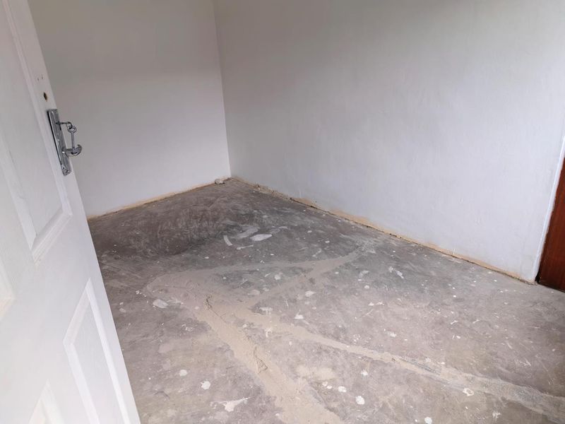 An empty bedroom featuring unfinished concrete flooring and plain white walls, ready for new floor finishes and interior design.
