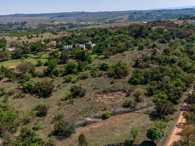 An aerial view of a large, undeveloped agricultural plot featuring natural vegetation, a dirt access road, and existing stone wall boundaries.