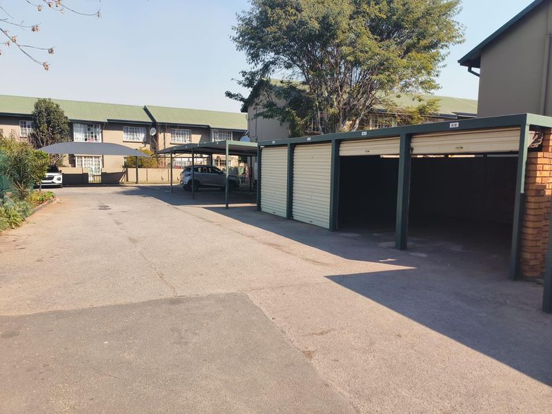 Exterior view of the apartment complex parking area featuring covered carports and individual lock-up garage units with asphalt paving.