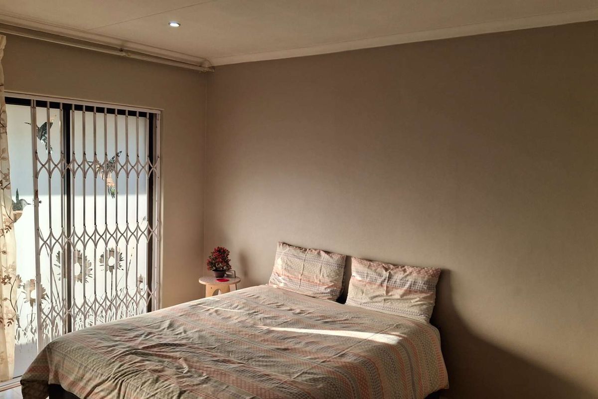 A bedroom featuring neutral wall tones, recessed downlighting, and a sliding glass door with an integrated security gate providing access to the exterior.