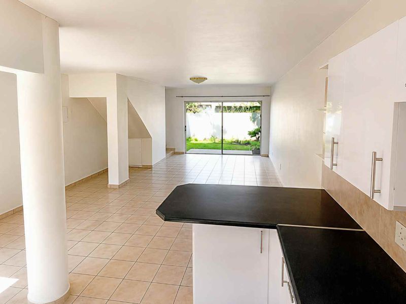 Spacious open-plan living and kitchen area featuring tiled floors, modern cabinetry, and large sliding doors leading to a private garden.