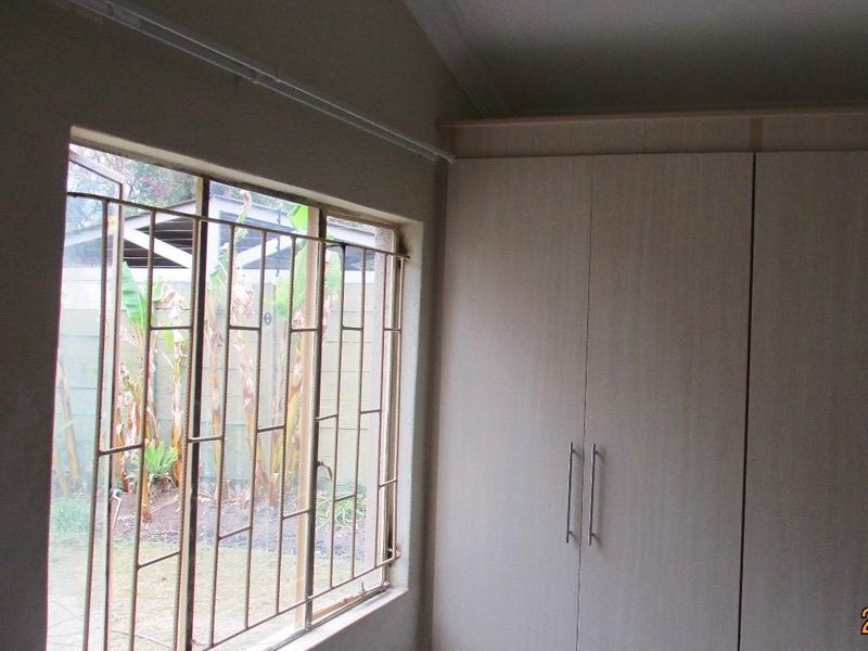 A bedroom featuring built-in wardrobes and a window fitted with security bars, offering a view of the rear garden area.