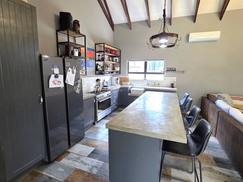 Spacious open-plan kitchen and living area featuring exposed timber beams, a large central island, modern cabinetry, and a farmhouse sink.
