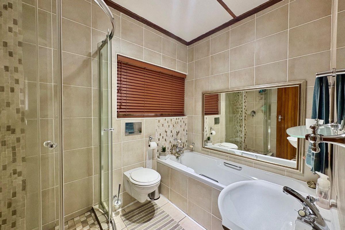 A well-maintained bathroom featuring a glass shower enclosure, built-in bathtub, wall-mounted toilet, and pedestal washbasin with neutral wall and floor tiling.