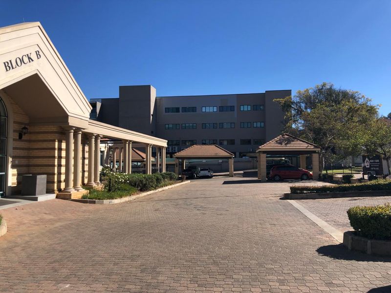 Exterior view of a commercial office complex featuring a paved driveway, covered parking bays, and a multi-story building facade.