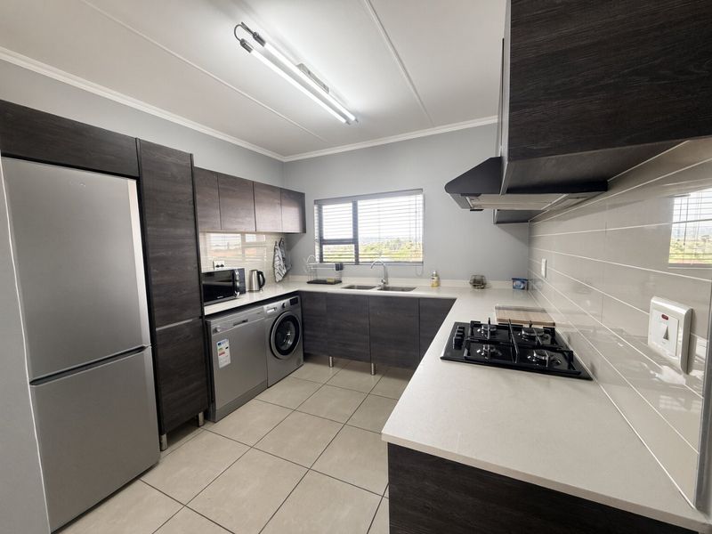 Modern kitchen featuring dark wood cabinetry, quartz countertops, gas hob, extractor fan, and tiled flooring with integrated appliance space.