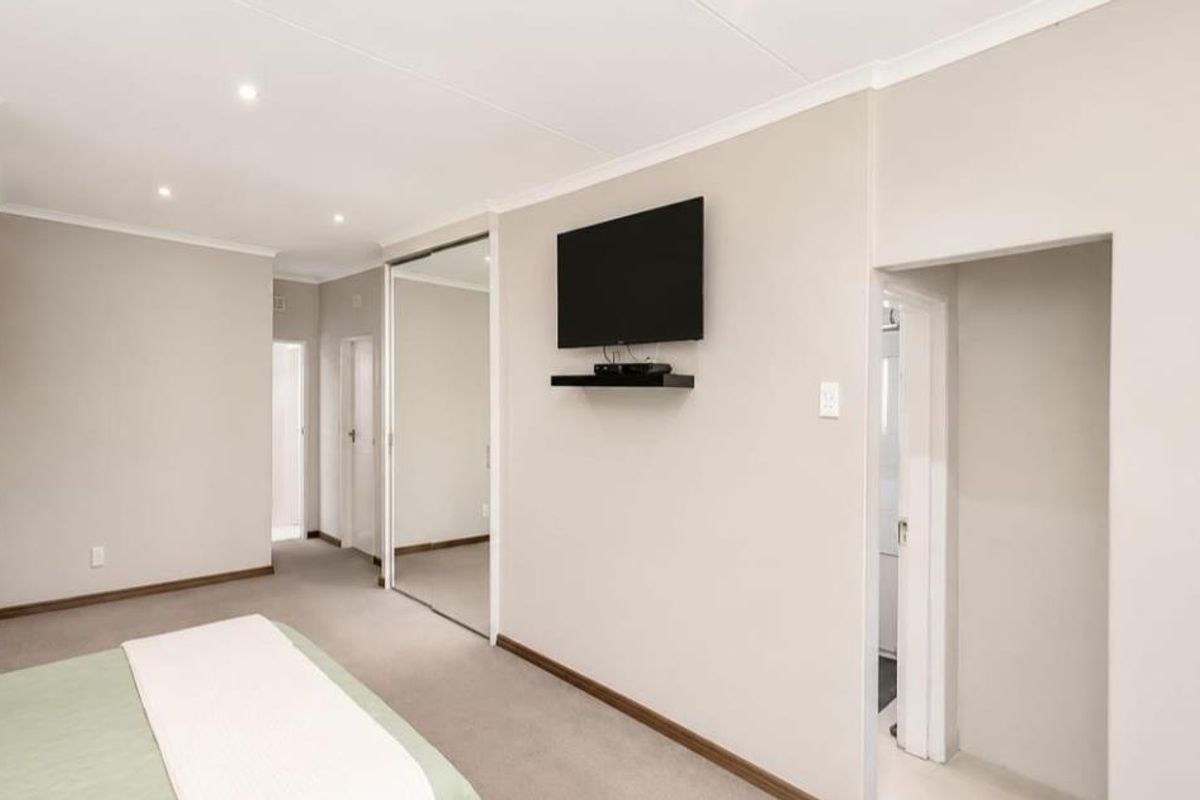 A well-maintained bedroom featuring neutral walls, recessed downlighting, and built-in cupboards with mirrored sliding doors.