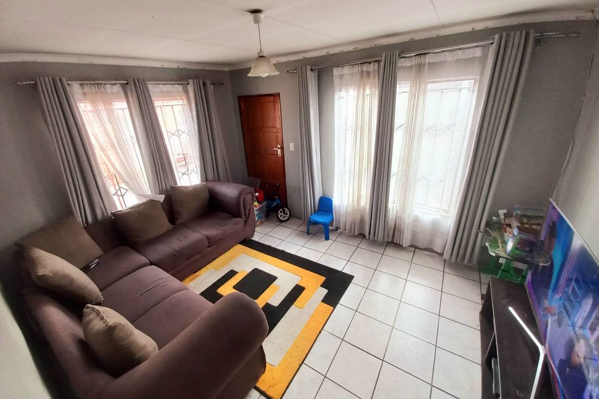 A living room featuring tiled flooring, large windows with security bars, and neutral wall tones, providing a functional and well-lit living space.
