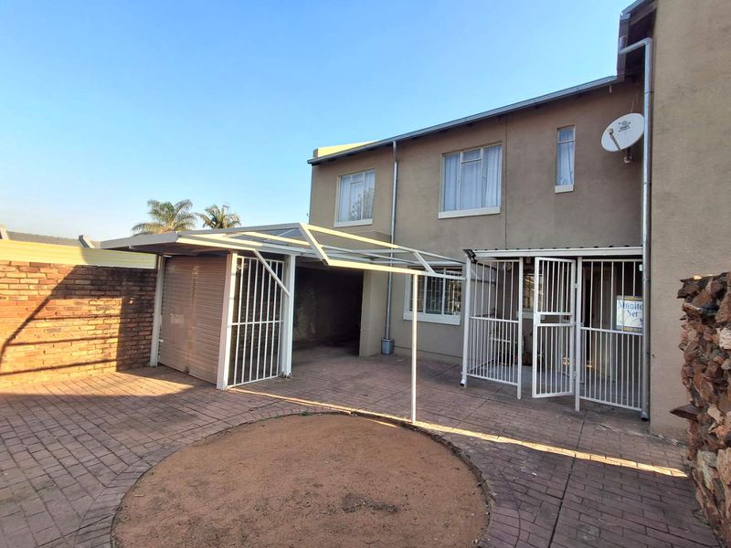 Rear exterior view featuring a paved courtyard, covered patio area, and secure metal gates attached to the main building structure.
