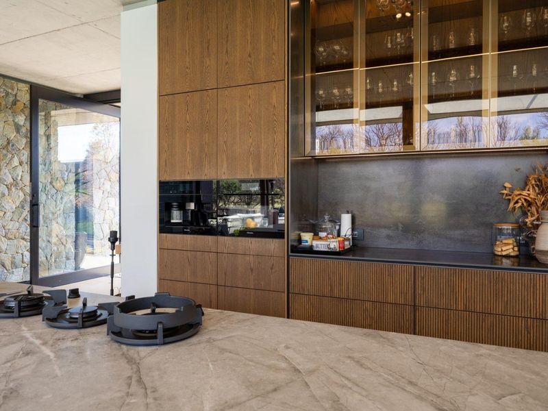Modern luxury kitchen featuring high-end integrated cabinetry, a stone island with a built-in gas hob, and elegant glass-fronted display units.