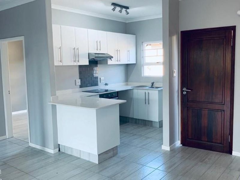 Modern open-plan kitchen featuring white cabinetry, quartz countertops, and tiled flooring, seamlessly integrated into the living area.