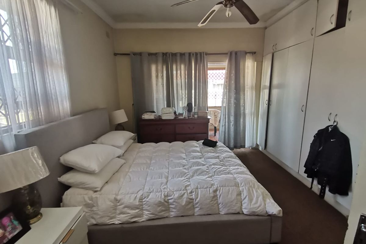 A spacious bedroom featuring built-in cupboards, a ceiling fan, and direct access to an outdoor area through glass doors.