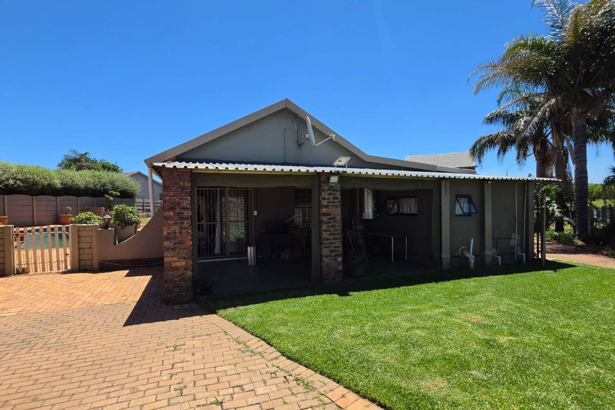 Rear view of the property featuring a covered patio area, brick pillars, paved driveway, and a well-maintained lawn.