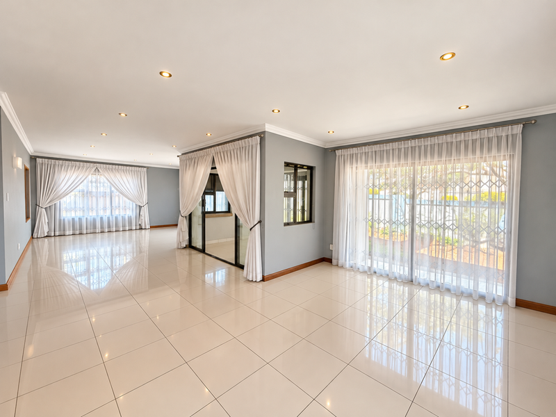 Spacious, light-filled living area featuring polished porcelain floor tiles, recessed downlighting, and large sliding glass doors with integrated security gates.