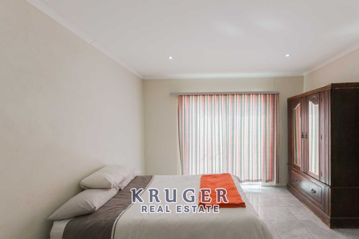 A spacious bedroom featuring tiled flooring, recessed ceiling lighting, and a large window with curtain track.