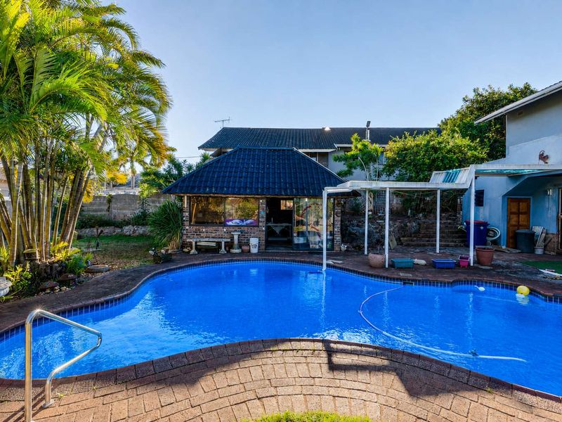 Outdoor pool area featuring a swimming pool with brick paving, a covered patio, and a detached brick outbuilding with a tiled roof.