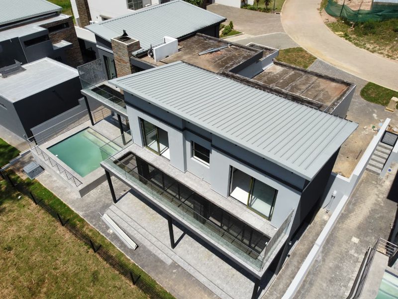 Aerial view of a modern cluster home featuring a metal roof, swimming pool, and glass-balustraded balcony with stone cladding accents.