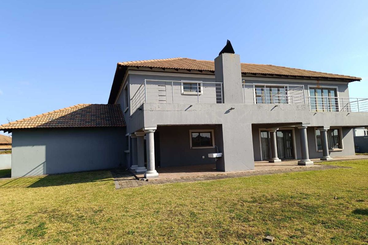 Rear view of a two-story house featuring a covered patio, upper-level balcony with metal railings, tiled roof, and a spacious lawn.