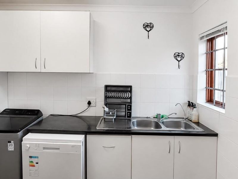 Functional laundry area featuring built-in white cabinetry, a double sink, tiled backsplash, and direct access to the exterior via a security gate.