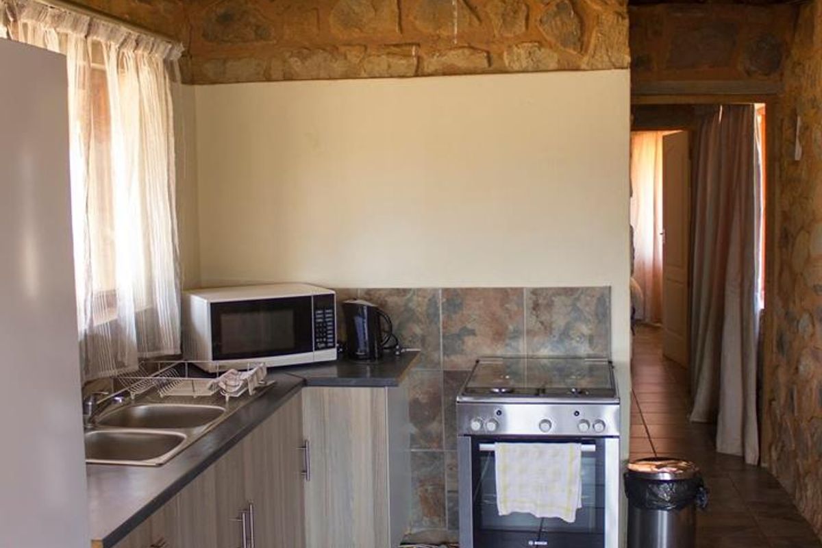 Rustic kitchen featuring a high thatched roof, stone walls, tiled flooring, built-in cabinetry, stainless steel oven, and double sink.