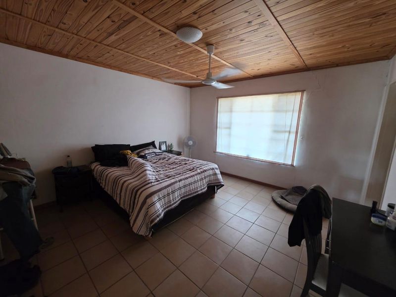 A bedroom featuring a timber-clad ceiling, ceiling fan, and tiled flooring, with visible wall cracks requiring maintenance.