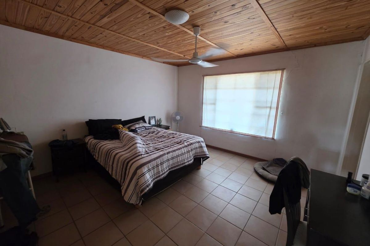 A bedroom featuring a timber-clad ceiling, ceiling fan, and tiled flooring, with visible wall cracks requiring maintenance.