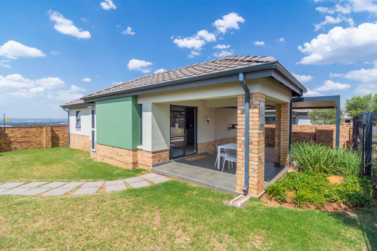 A well-maintained rear exterior view featuring a covered patio with brick pillars, tiled flooring, and a landscaped garden with a paved walkway.