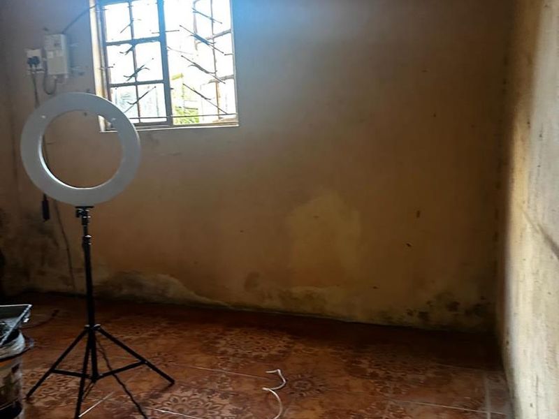 An empty bedroom featuring tiled flooring and a window with security bars, showing significant signs of wall wear and dampness requiring maintenance.