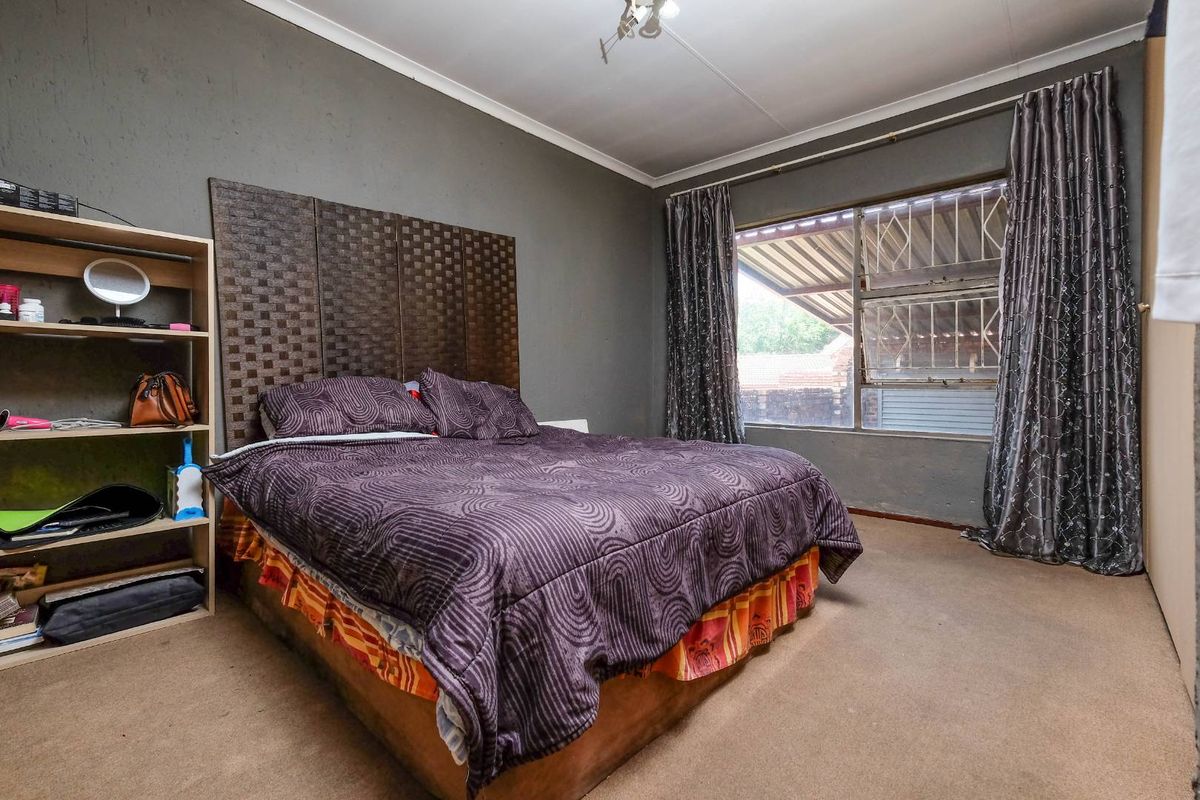 A bedroom featuring carpeted flooring, a large window with security bars, and a neutral wall finish, offering a functional space for rest.