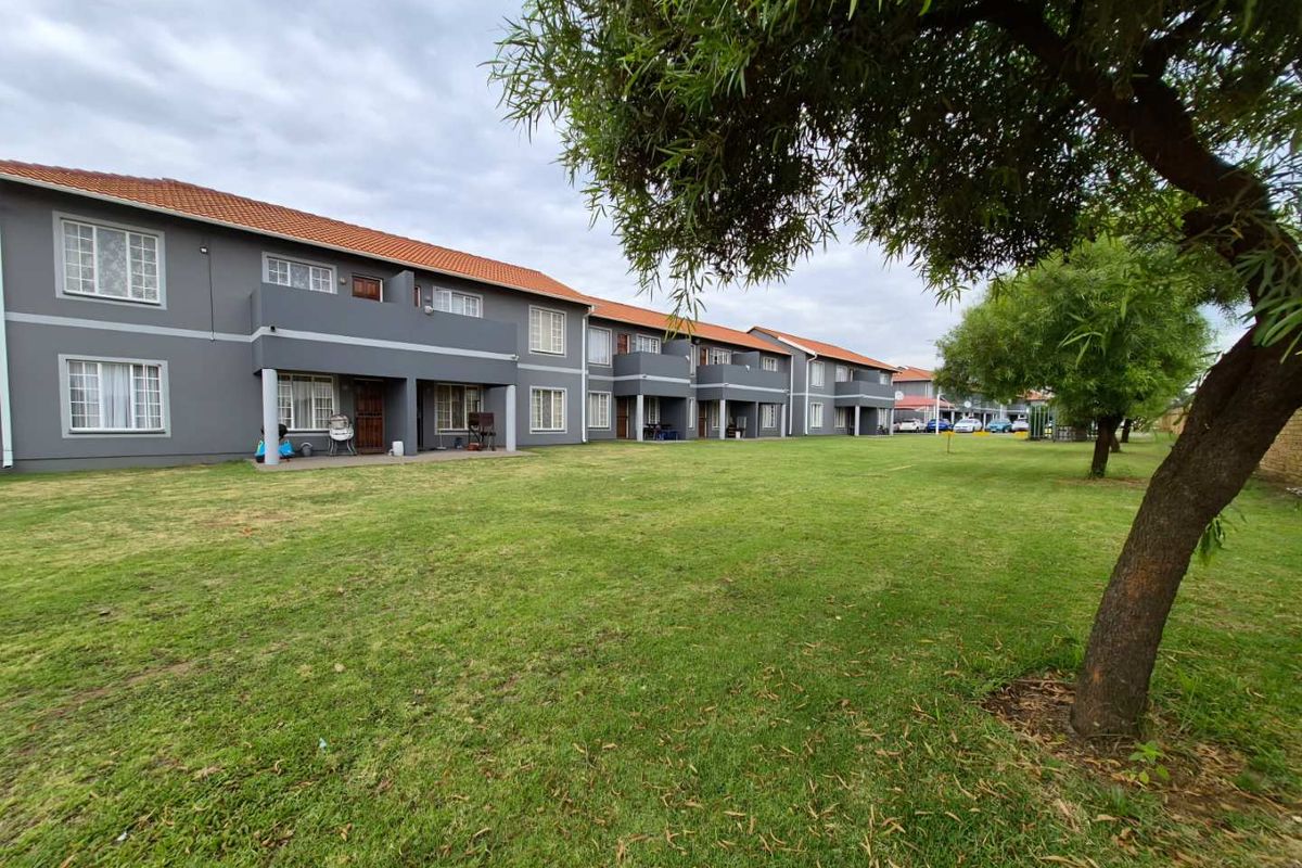 A view of the apartment complex exterior featuring a well-maintained lawn, paved walkways, and covered patio areas for ground-floor units.