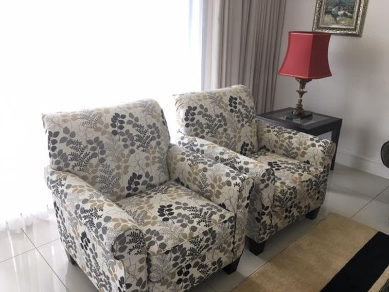 A bright living area featuring neutral tiled flooring and large windows with floor-to-ceiling curtains, providing a clean and well-maintained space.
