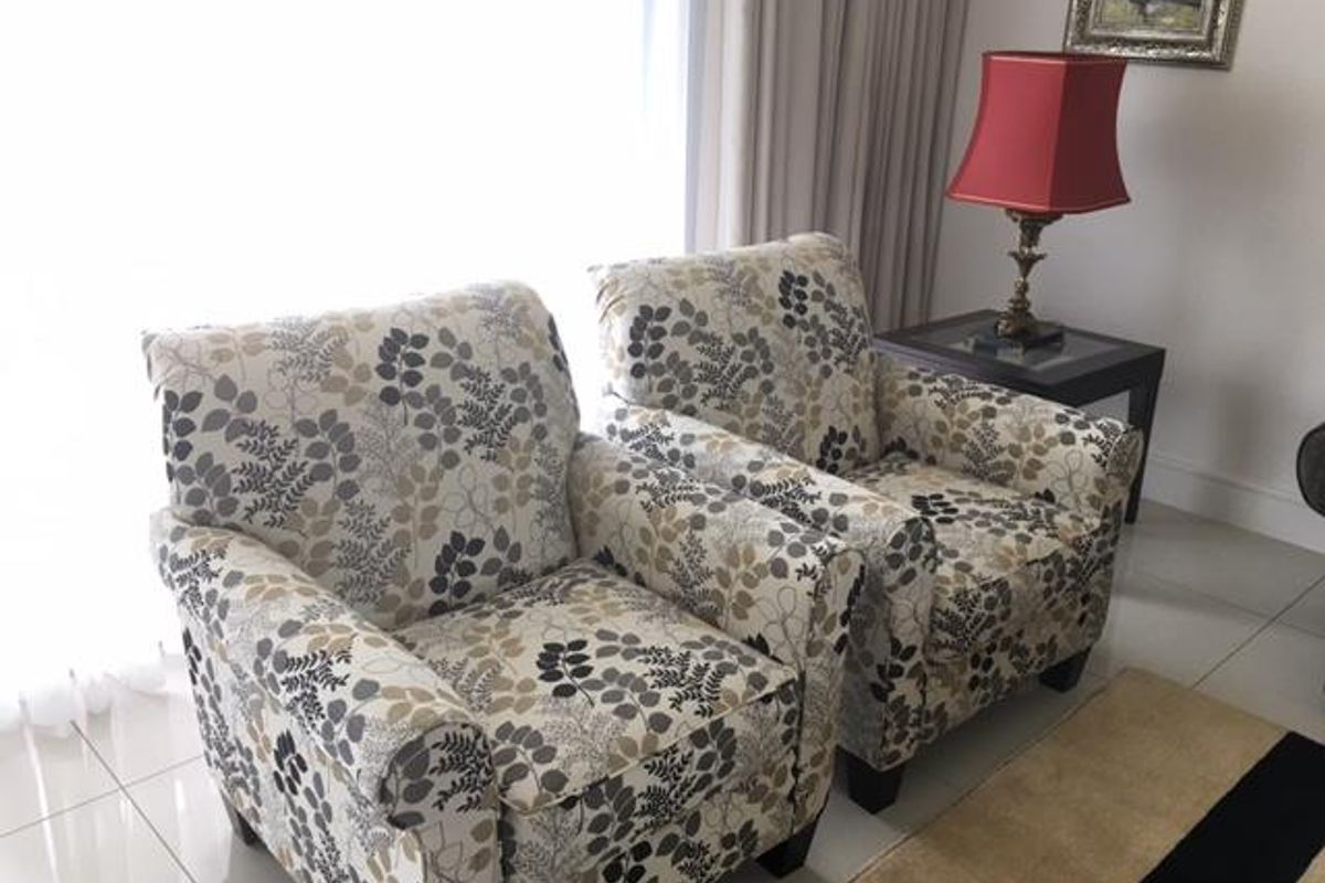 A bright living area featuring neutral tiled flooring and large windows with floor-to-ceiling curtains, providing a clean and well-maintained space.