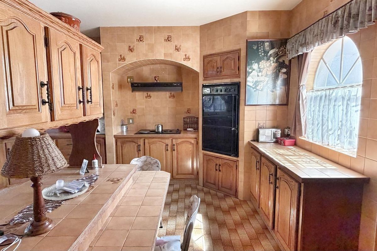 A traditional kitchen featuring extensive wooden cabinetry, tiled countertops, a built-in oven, and a hob with an extractor fan.