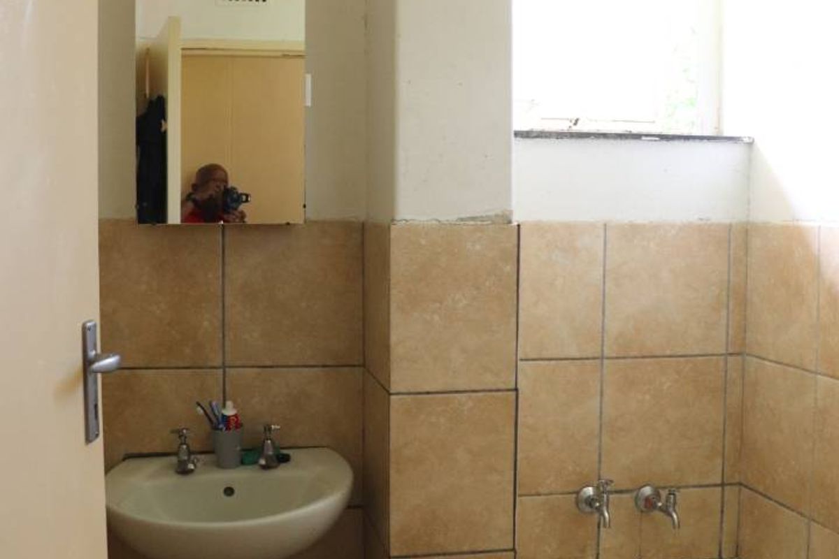 A dated bathroom featuring a standard bathtub, wall-mounted basin with exposed plumbing, and neutral ceramic wall tiles.