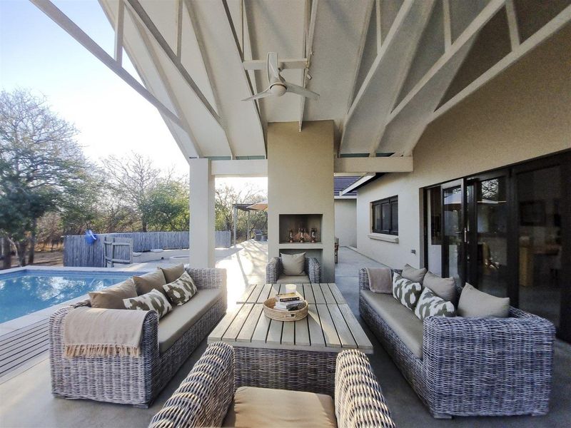 A spacious covered patio featuring a built-in fireplace, exposed rafters, and a ceiling fan, overlooking a private swimming pool.
