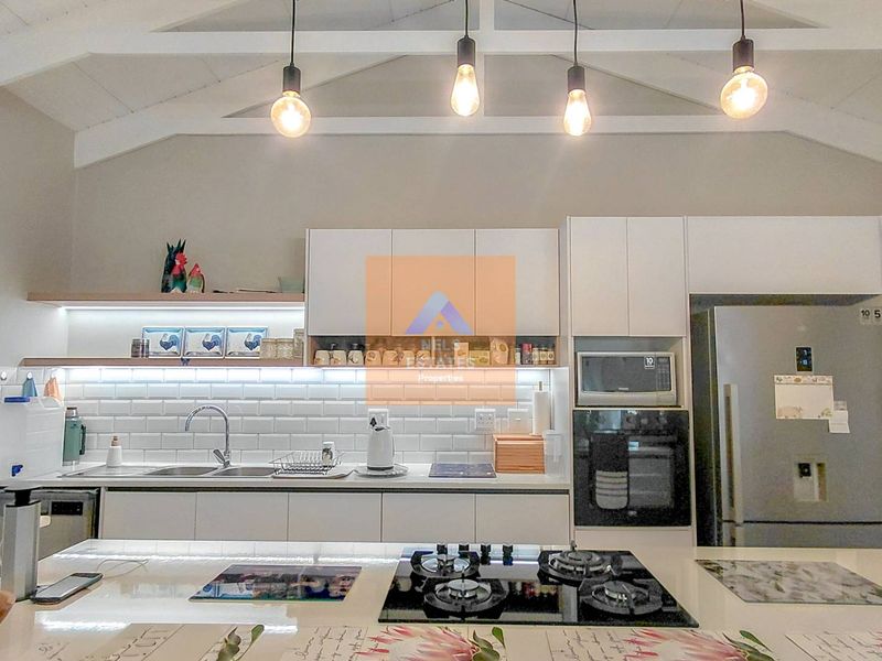 Modern kitchen featuring white cabinetry, subway tile backsplash, built-in appliances, gas hob, and an exposed beam ceiling with pendant lighting.
