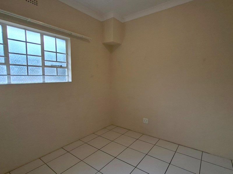 An empty bedroom featuring neutral wall paint, tiled flooring, and a steel-framed window with textured glass.
